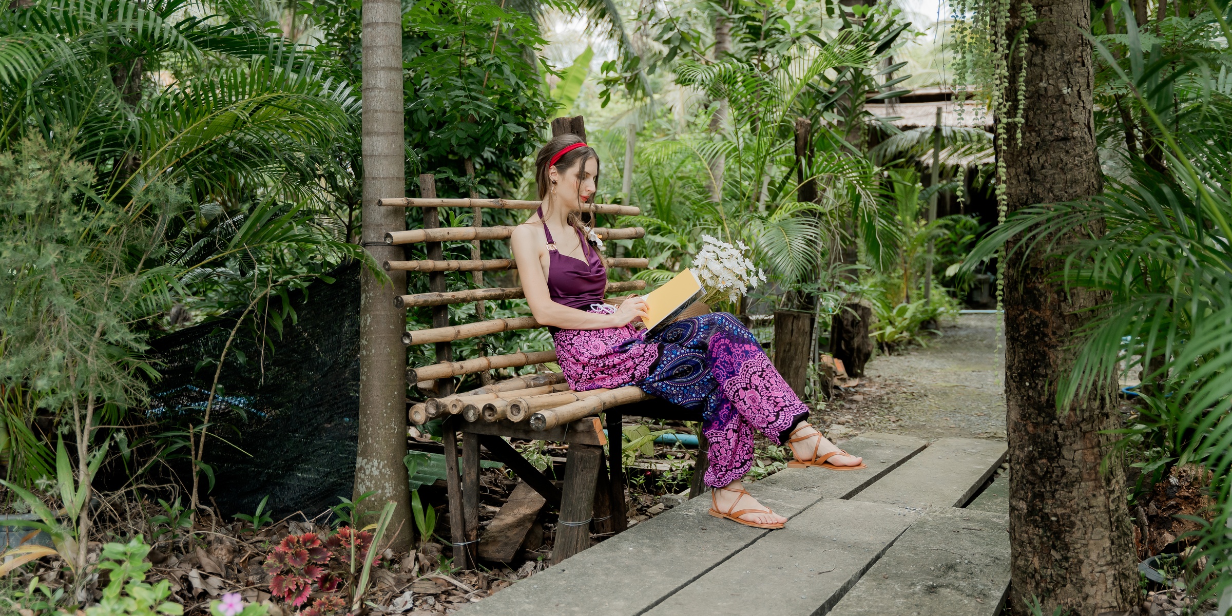 Woman reading in a tropical garden wearing pink and blue patterned pants